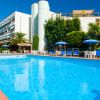 Piscina azzurra circondata da sedie a sdraio blu e palme, con un grande edificio sullo sfondo.