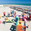 Bambini giocano su una spiaggia con scivoli colorati, mare in lontananza.