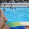 Gambe su lettino in piscina con persone che nuotano.
