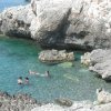 Persone che nuotano in un mare roccioso e limpido.