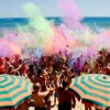 Festa colorata sulla spiaggia con persone e ombrelloni arancioni e verdi.