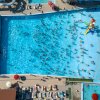 Piscina affollata vista dall'alto con scivoli d'acqua a sinistra e lettini intorno.