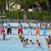 Persone in una piscina bassa si divertono, alcune partecipano a una lezione guidata.