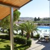 Vista su una piscina affollata circondata da palme e verde, con un campo collinare sullo sfondo.