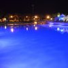 Piscina illuminata di notte con luci blu, vegetazione e luci sullo sfondo.