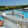 Persona su scivolo d'acqua, vista di piscina affollata e palme.
