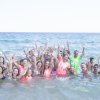 Un gruppo di persone che sorridono e alzano le mani nell'acqua di mare.