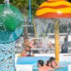 Un recipiente verde versa acqua in piscina, mentre persone nuotano sullo sfondo.