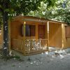 Bungalow in legno con veranda, circondato da alberi ombrosi e una bicicletta parcheggiata.