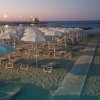 Spiaggia al tramonto con ombrelloni bianchi in fila.