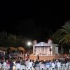 Spettacolo serale all'aperto con pubblico seduto davanti a un palco.
