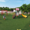 Parco giochi con altalene, scivolo e dondoli su prato verde.