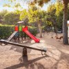 Parco giochi con altalena e scivolo rosso.