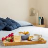 Vassoio con colazione, fiori e caffè su un letto con cuscini blu.