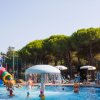 Piscina con giochi d'acqua e scivolo colorato, persone che nuotano.