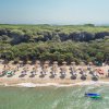 Spiaggia con ombrelloni e vegetazione rigogliosa sullo sfondo.