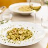 Piatto di gnocchi con gamberi e pistacchi, bicchiere di vino bianco accanto.
