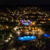 Vista notturna di un resort con piscine illuminate e capanne sparse su una collina.