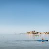 Persona in kayak azzurro su un mare calmo, con un villaggio costiero sullo sfondo.