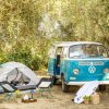 Furgone Volkswagen con tenda e attrezzatura da campeggio in un boschetto.