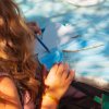 Bambina che colora un disegno a forma di farfalla blu su un tavolo soleggiato.