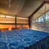 Interno di una tenda con letto matrimoniale, copriletto blu e lampada accesa.