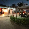 Esterno di un bar illuminato di sera con gazebo e sedie sotto le palme.