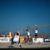 Giocatori di beach volley in azione sulla sabbia, pubblico sullo sfondo.