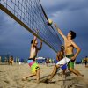 Partita di beach volley su una spiaggia con tre giocatori sotto un cielo nuvoloso.