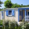Casetta con persiane blu, circondata da piante e alberi, in un ambiente verde.
