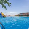 Una piscina con scivoli gialli, persone che nuotano e sedie a sdraio sullo sfondo.