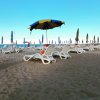 Sedie a sdraio e ombrelloni su una spiaggia sabbiosa sotto un cielo azzurro.
