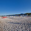 Spiaggia di ciottoli con ombrelloni blu e gialli e un mare calmo sullo sfondo.