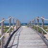 Passerella in legno con corde, che conduce verso il mare.