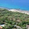 Veduta dall'alto di una costa, mare blu, vegetazione e bungalow.