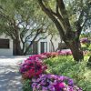 Giardino con fiori colorati sotto ulivi, accanto a un edificio bianco.