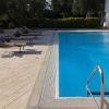 Bordo piscina con sdraio nere, scaletta metallica e vegetazione sullo sfondo.
