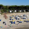 Spiaggia con ombrelloni gialli e lettini blu, alberi e camper sullo sfondo.