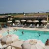 Piscina all'aperto con ombrelloni bianchi, lettini e persone che nuotano.