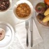Colazione con cereali, cappuccino e frutta su una tovaglia bianca.