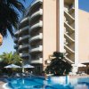 Edificio moderno con balconi curvi, piscina circondata da sedie a sdraio, ombrelloni e palme.