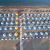 Vista aerea di una spiaggia con file ordinate di ombrelloni blu e gialli.