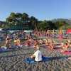 Persone fanno yoga su una spiaggia, circondate da ombrelloni e alberi.