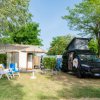 Camper e sedie fuori da una casetta in un campeggio verde.