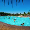 Persone in una grande piscina all'aperto con ombrelloni sullo sfondo.