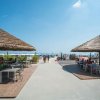 Due tettoie di paglia su una terrazza fronte mare con tavoli e persone sedute.