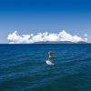 Persona su una tavola da paddle sul mare sotto un cielo azzurro con nuvole bianche.