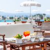 Tavolo esterno con aperitivi, sedie in legno e vista su piscina e ombrelloni bianchi.