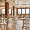 Ristorante luminoso con sedie e tavoli bianchi. Ampie finestre e piante decorative.