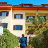 Persona cammina verso un edificio a tre piani con balconi e una palma in giardino.